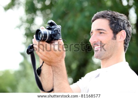 Happy relaxed man looking at the screen of his DSLR camera as he takes a photograph