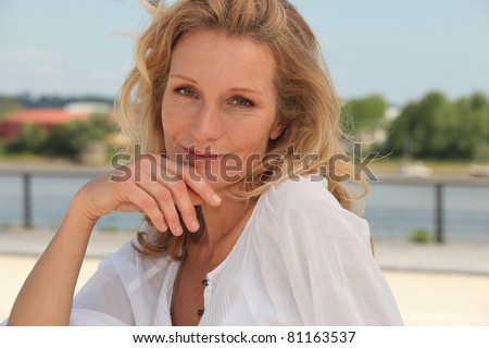 Smirking woman with hand on chin sitting outside
