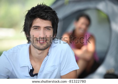 Young man camping with his girlfriend and tent out of focus in the background