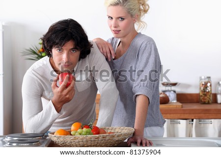 a couple in the kitchen, the man is eating an apple