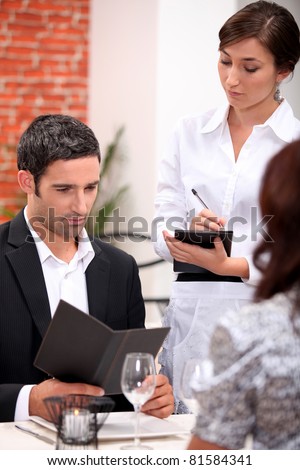 a man and a woman ordering at the restaurant, a waitress is writing the order