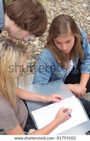 Three young people, one of them writing in a binder on her lap.