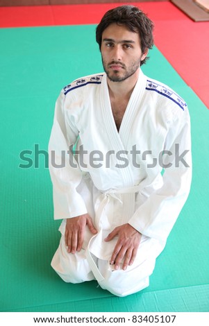Adult male kneeling on mat in martial arts clothing