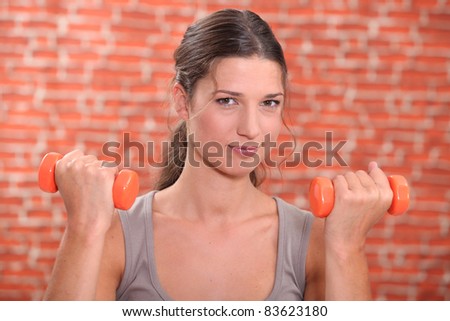 Young woman using hand weights in front of a red brick wall