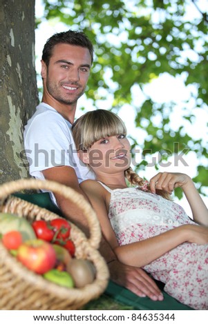 Couple sat by tree with basket of fresh produce