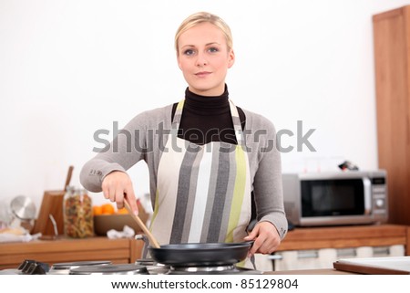 30 years old blonde woman is cooking with a stove and a spatula in her kitchen