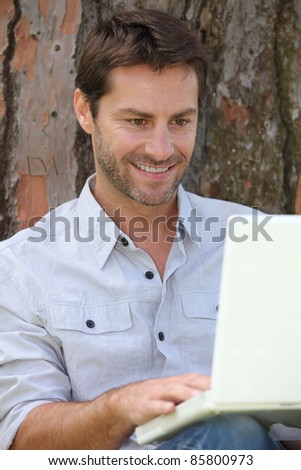 Man sat by tree with laptop computer