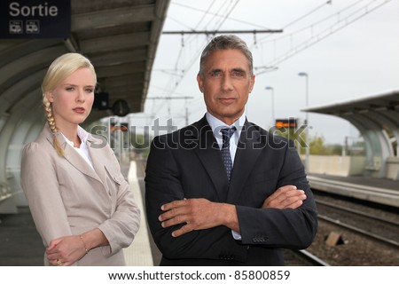 a blonde woman and a mature man well dressed in a train station