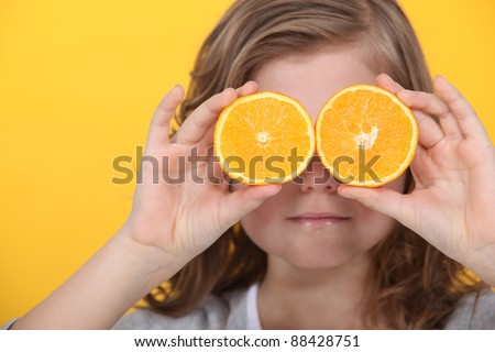 Little girl covering eyes with slices of orange
