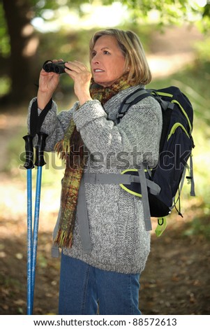 60 years old blonde woman is contemplating landscapes with binoculars, she\'s wearing warm clothes and using a crook