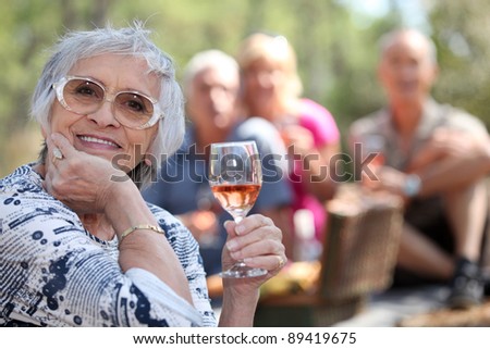 Senior woman enjoying a glass of rose wine with friends on a picnic