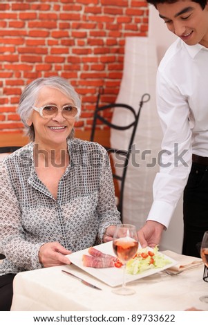 Young waiter serving an older woman in a restaurant