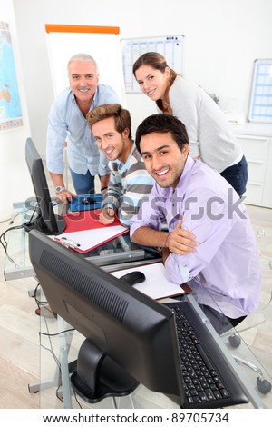 Four smiling people gathered round a computer in a classroom