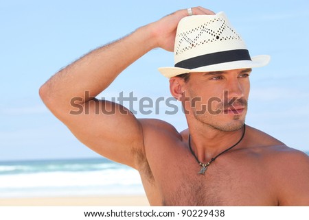 Muscular man posing on the beach in a panama hat