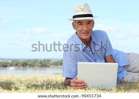 Senior man using a laptop computer on a riverbank