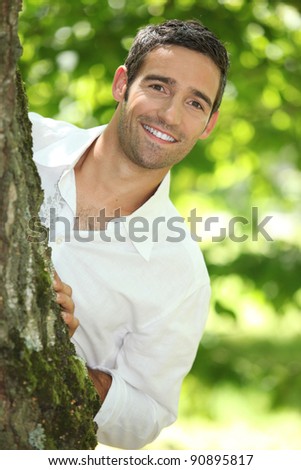 Peekaboo. Man in a white shirt peering round a tree.