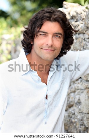 Handsome man with long hair standing by an old stone wall