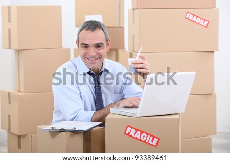 a business man drinking doing computer among cardboard boxes