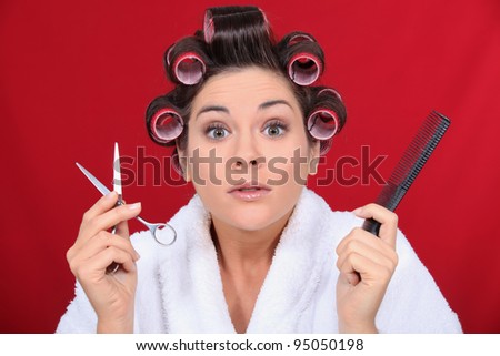 Woman with her hair in curlers holding scissors and a comb