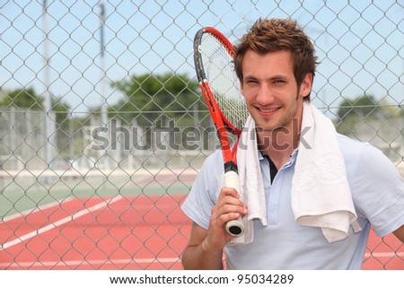 A tennis player posing in front of a tennis court with his racket.