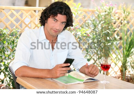 Man sitting at an outdoor cafe table with a cellphone and glass of rose