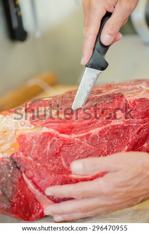 Butcher wearing a meat glove whilst preparing cut of beef