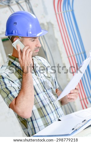 Man on building site, looking at plans, talking on cellphone