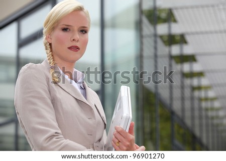 Blond businesswoman holding laptop computer outside glass building