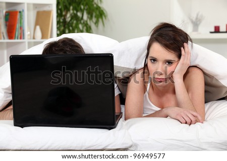 Man using laptop in bed and young woman bored