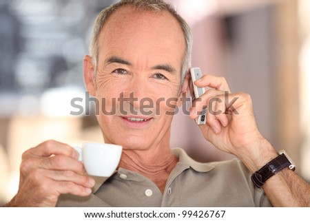 Grey haired man drinking coffee and speaking on mobile telephone