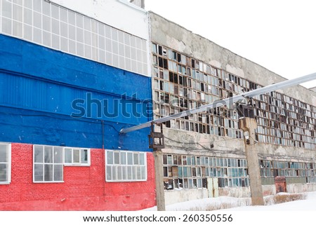 Two industrial buildings old and new. Old with broken windows. New painted in white, blue and red.