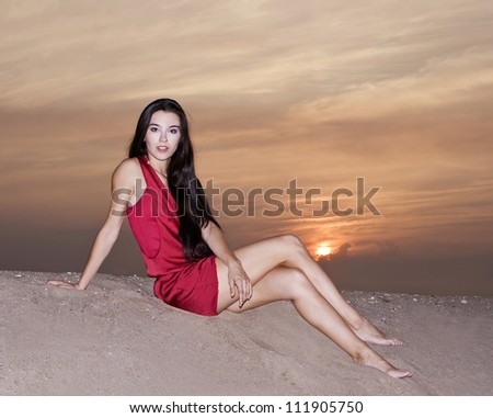 Cute female in red dress posing at the desert in sunset