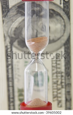 Closeup view of sand flowing through an hourglass on the background money