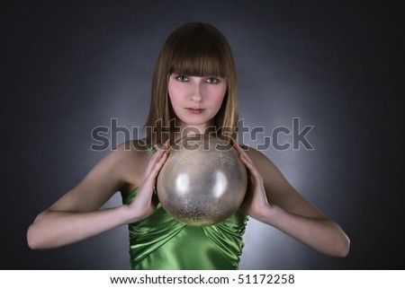 stunning woman in green dress with gold sphere in hand  over black background