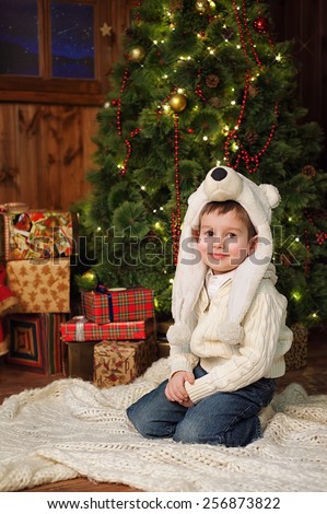 the little 4years boy sitting near a Christmas tree in a wooden country style house.