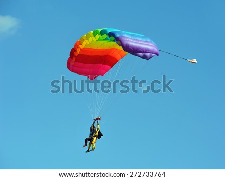 Tandem rainbow-colored parachute against clear blue sky