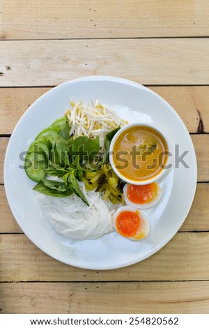Rice noodles in (with) fish curry sauce / Traditional Thai cuisine, rice vermicelli   served with boiled egg  and vegetable  on wood table.Selective Focus.