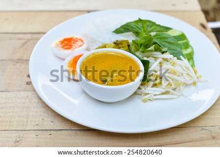 Rice noodles in (with) fish curry sauce / Traditional Thai cuisine, rice vermicelli   served with boiled egg  and vegetable  on wood table.Selective Focus.