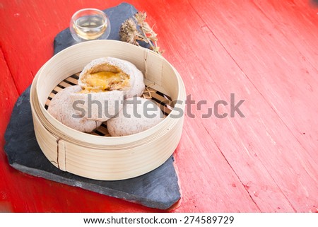 Chinese steamed bun and sweet creamy stuff set with  a cup of hot tea  on black stone and red background