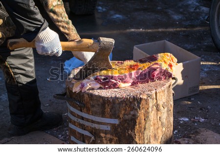 A butcher uses an axe to cut fresh raw beef ready to sell at a local market
