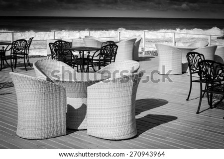 Empty wicker and black iron chairs wait for tourists in the cloudy sun cast sky