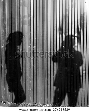 Photographer taking a photo of a woman casting shadows on red metal wall in black and white