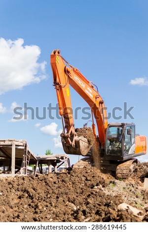 UFA/BASHKORTOSTAN - RUSSIA 13th June 2015 - Orange digger excavates soil in preparation for new apartments for young families in Ufa city Bashkortostan Russia in June 2015