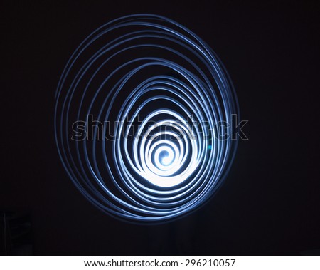 Single swirling spiral painted in blue light in the darkness