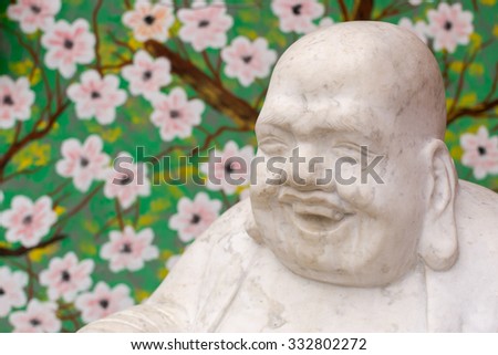 Laughing buddha statue in white stone with a green floral background