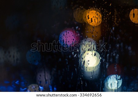 Car headlights and street lights at night create bokeh style defocused blurs as rain water reflects off of windscreen glass