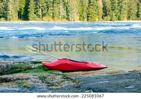 Red whitewater kayak with a paddle on a rocky shore against river