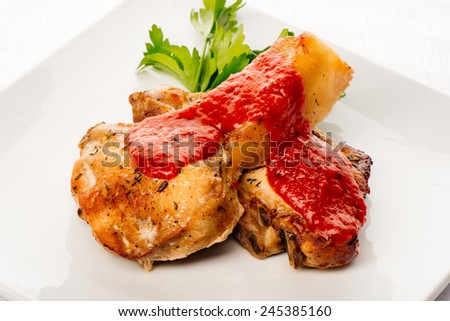 Roasted pork ribs with tomato sauce, parsley and spices laying on white plate, shot on white background