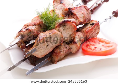 Pieces of fresh fried meat on skewers, laying on a white plate with tomato and dill on white background