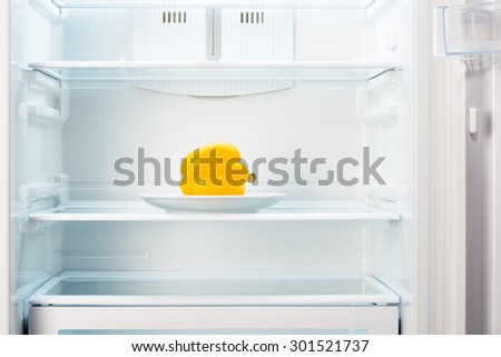 Yellow pepper on white plate in open empty refrigerator. Weight loss diet concept.